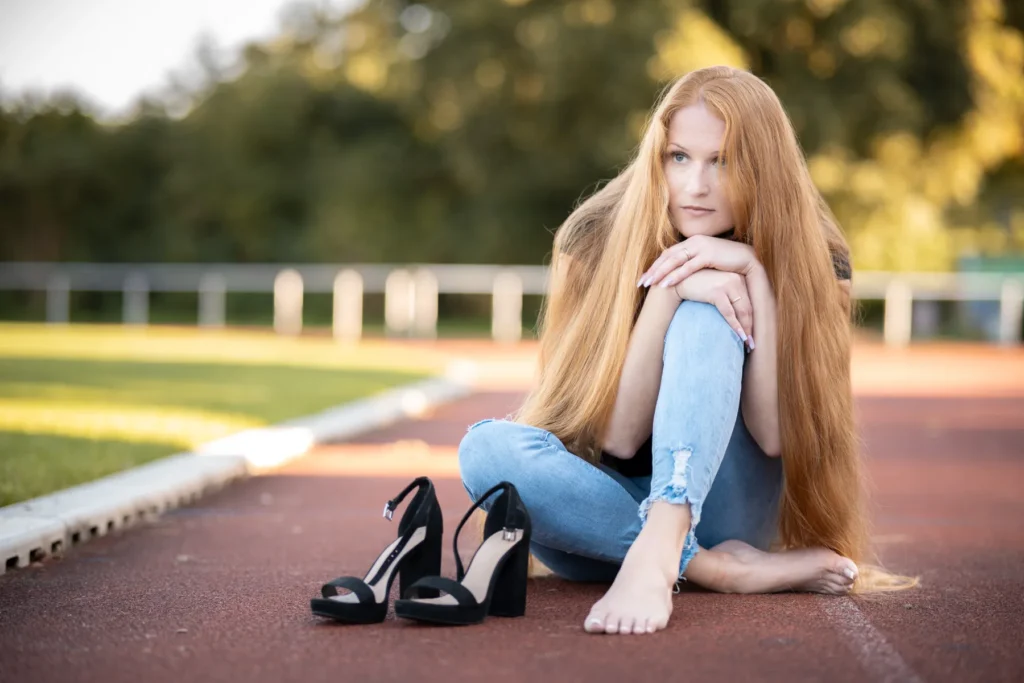 Portrait einer barfüßigen Frau mit sehr langen roten Haaren auf einer Laufbahn sitzend