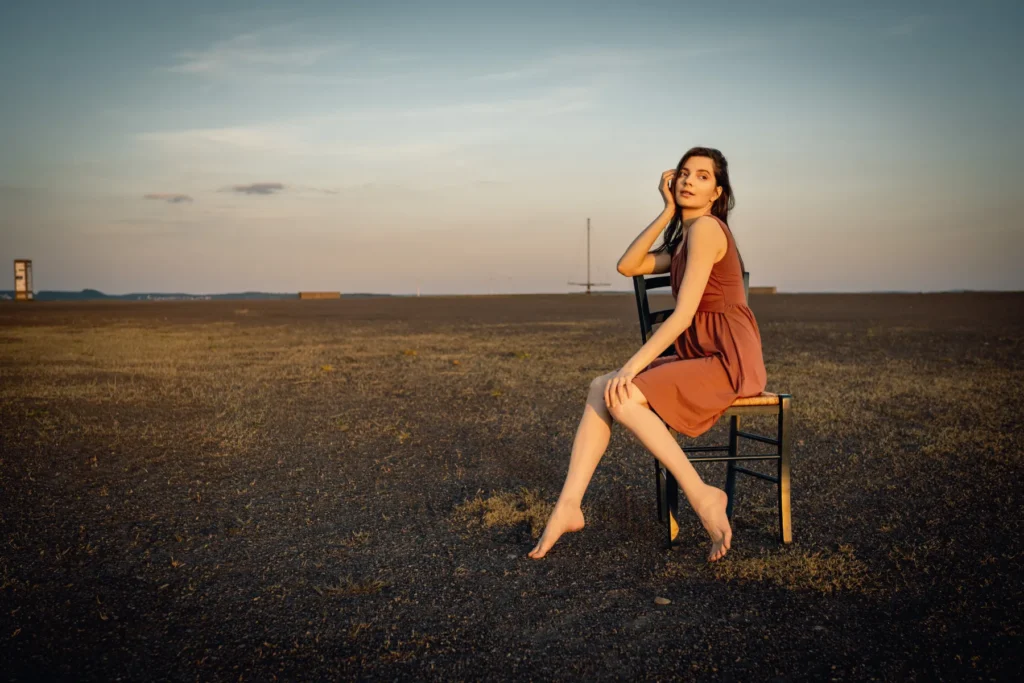 Portrait einer jungen Frau auf einem Stuhl sitzend kurz vor Sonnenuntergang - atmosphärische Outdoor-Aufnahme