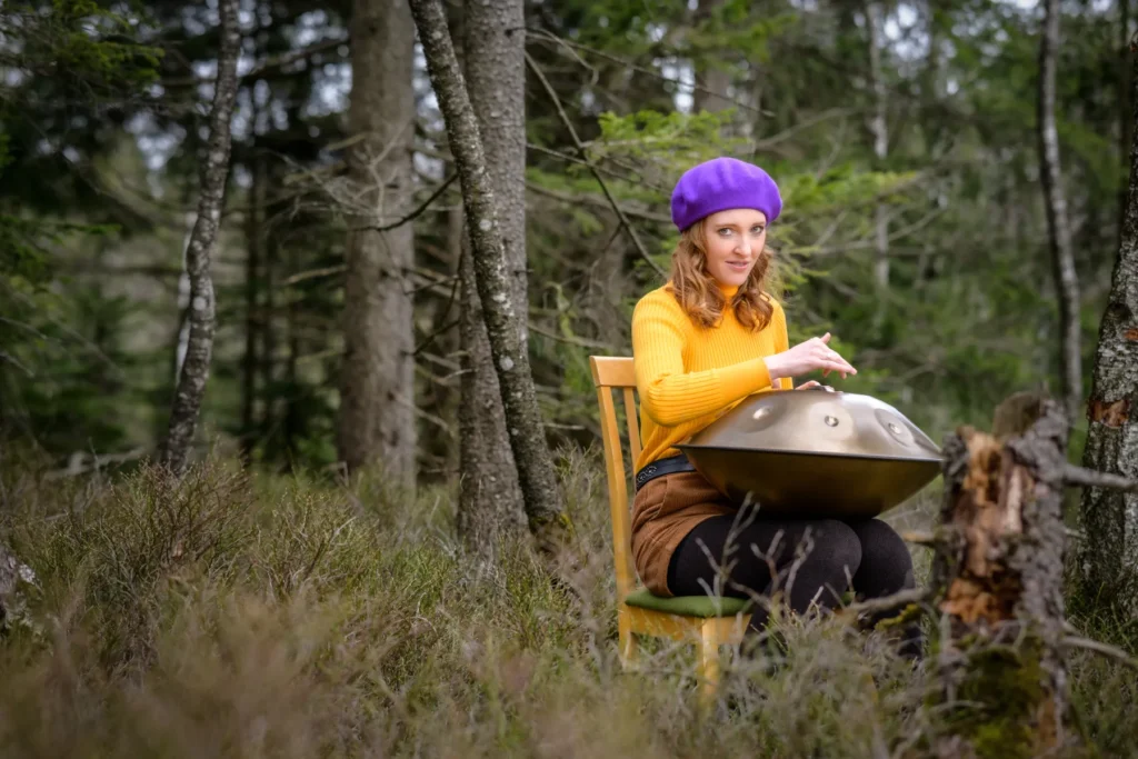 Porträt einer sitzenden Frau mit Baskenmütze und Handpan im Wald